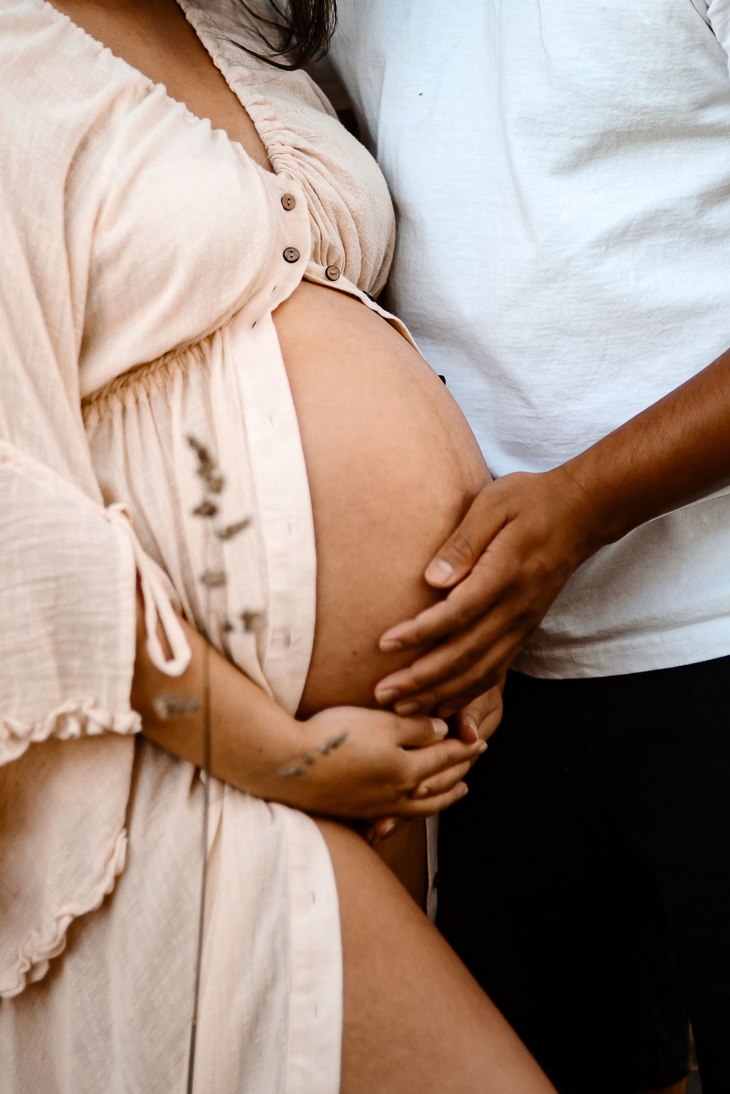A tender pregnancy moment captured as hands gently rest on a pregnant belly wearing a flowy beige dress.