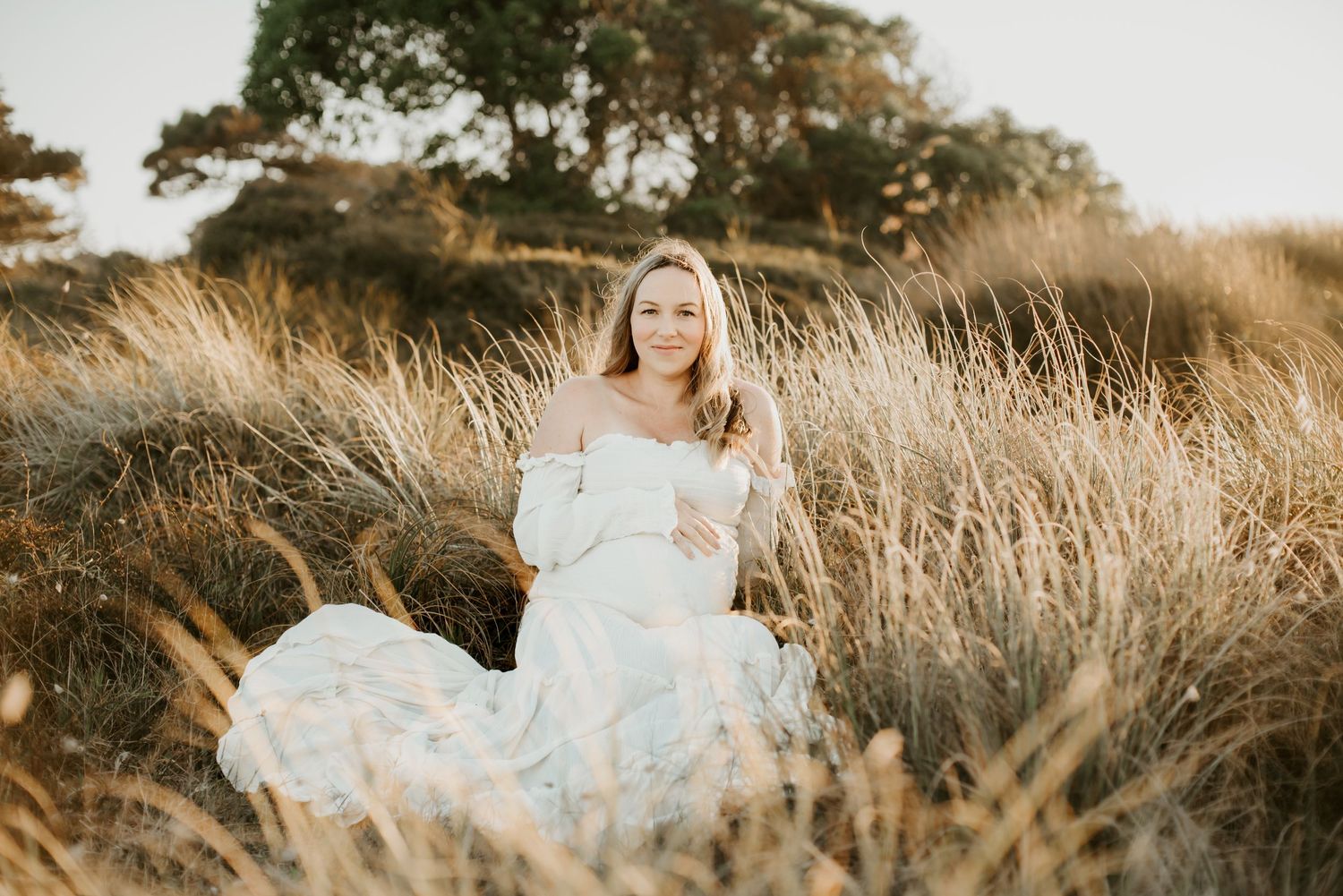Dreamy outdoor maternity session in white flowing dress surrounded by golden field grass.