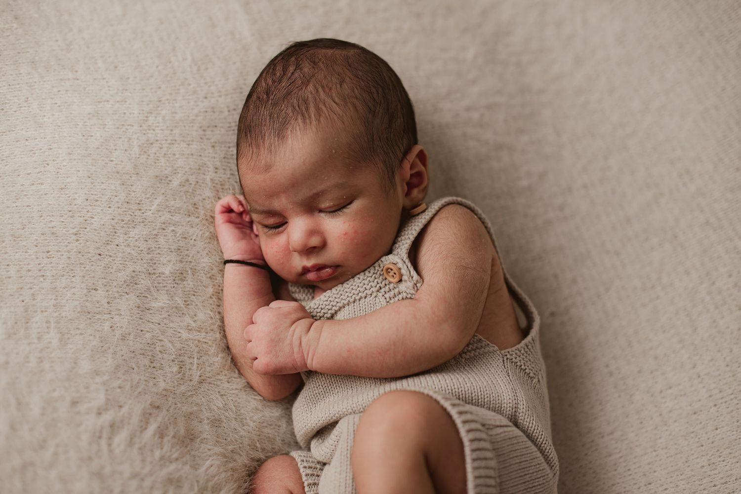 Sleeping newborn baby in beige outfit on cream background.