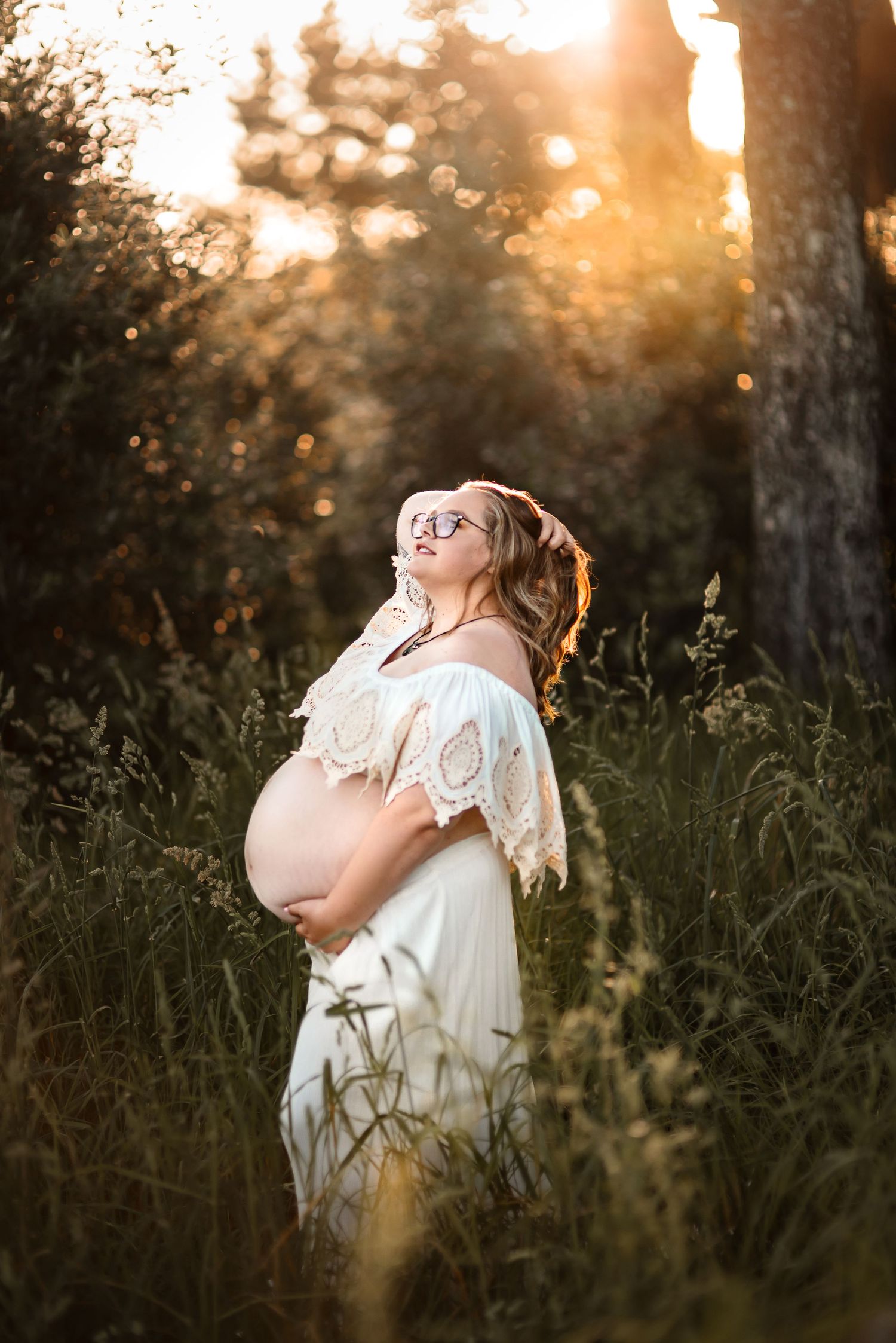 A dreamy maternity portrait in a white dress during golden hour among wildflowers.