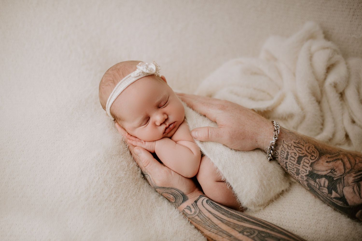 Delicate newborn photography featuring sleeping baby wrapped in soft white fabric.