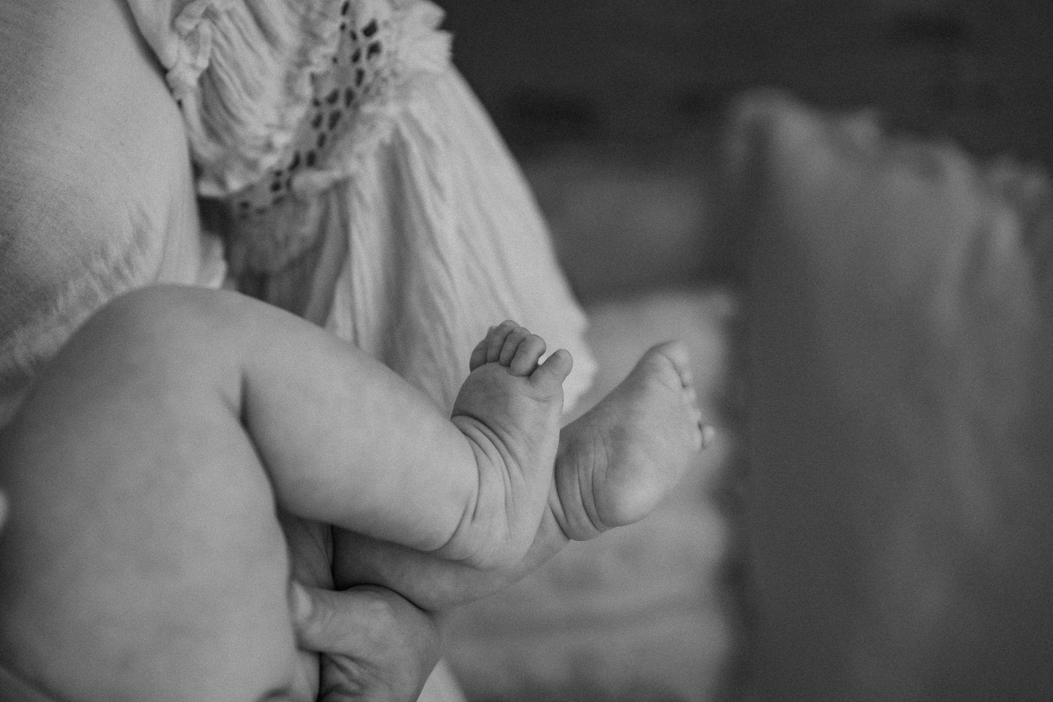 Close-up black and white image of a tiny baby's foot against soft fabric.