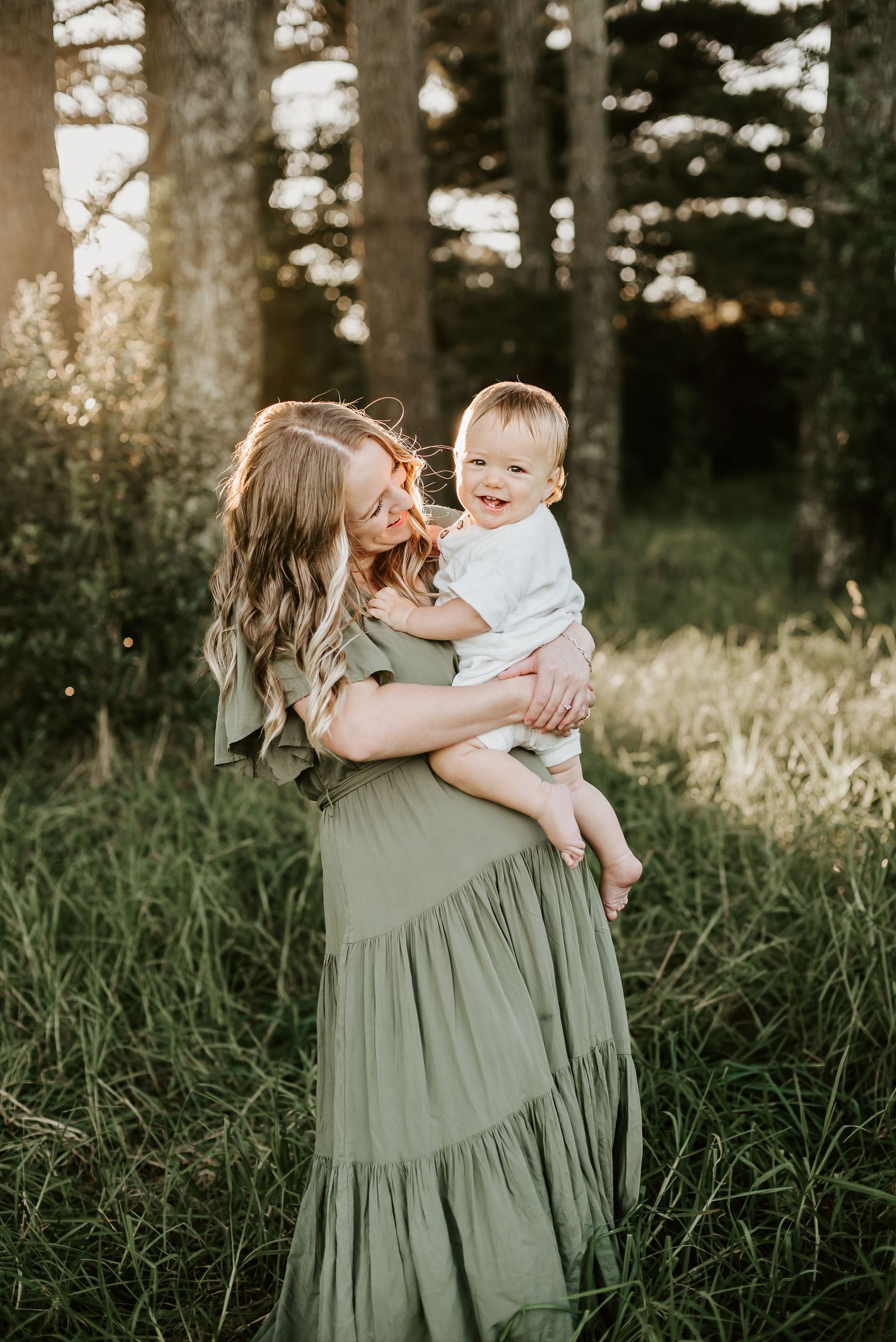 Sweet outdoor family moment captured in a field with forest backdrop at golden hour.