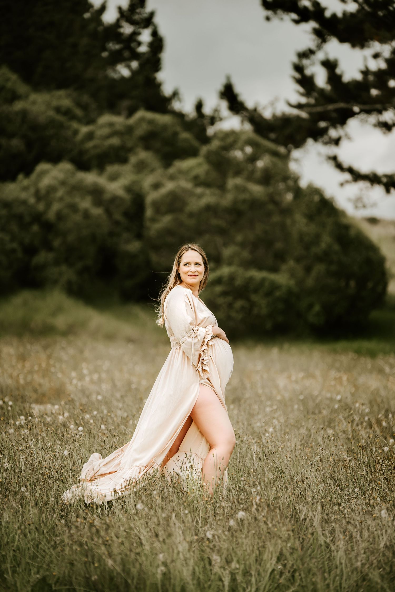Flowing dress maternity photoshoot in a dreamy field at sunset with soft lighting and natural scenery.