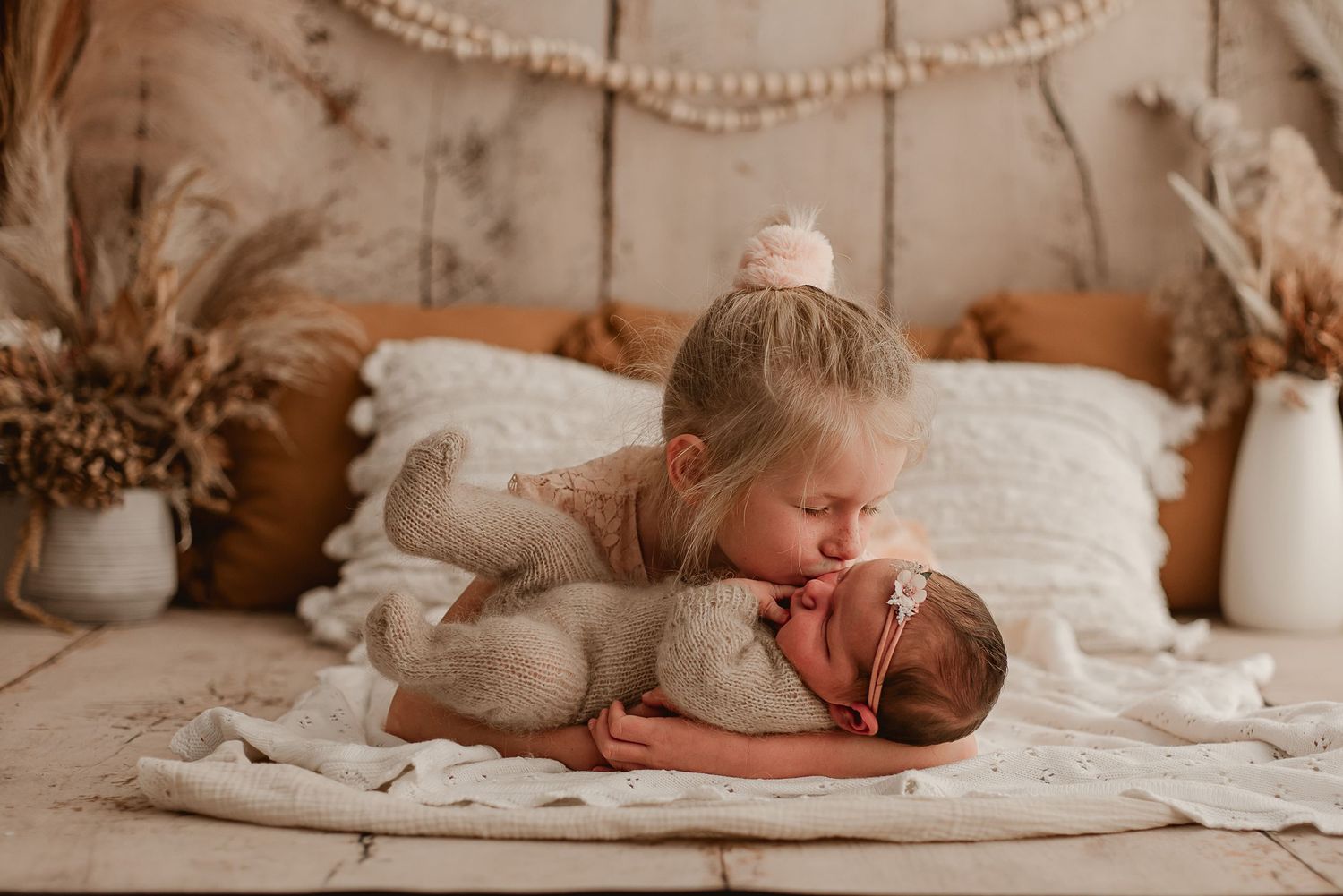 Siblings share a tender moment on cream bedding with neutral boho decor.