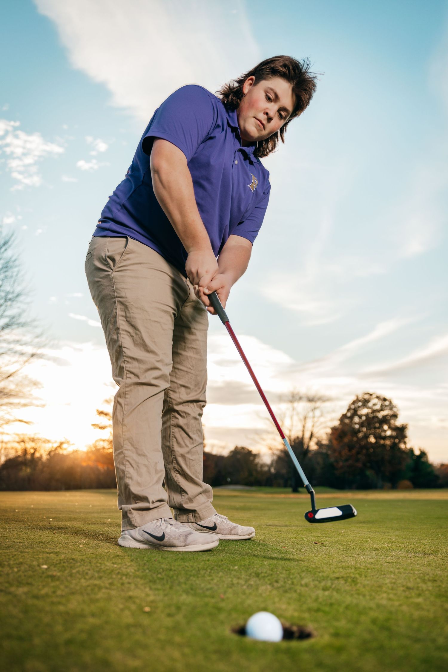 Golfer practicing putting on green course during golden hour sunset.