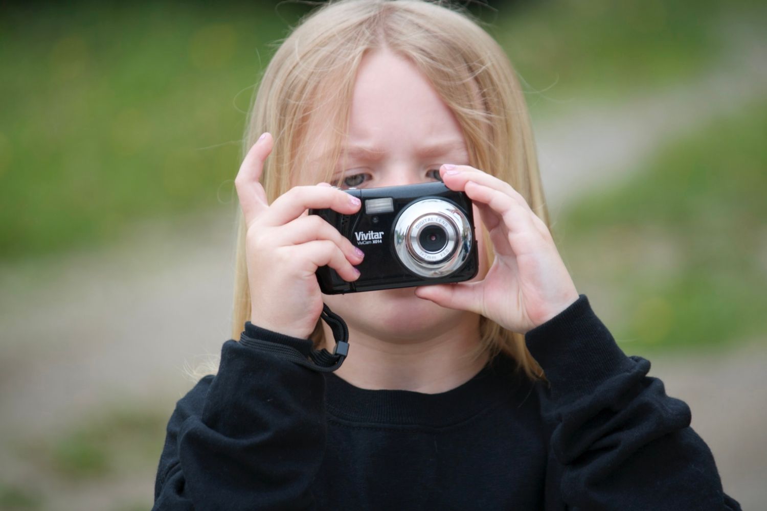 Person holding a vintage camera up to take a photo outdoors.