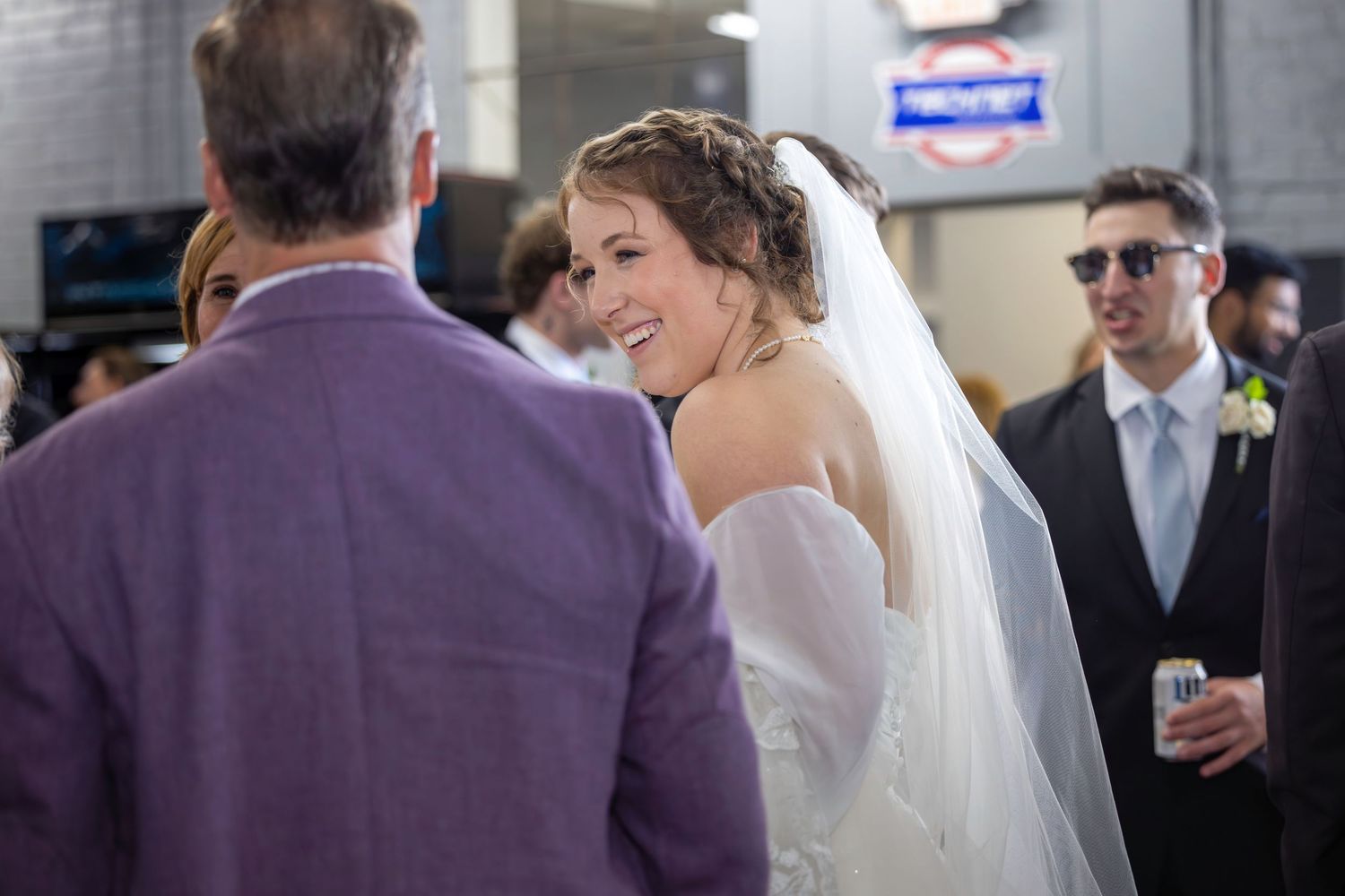 Wedding guests interact during an indoor reception with natural lighting.