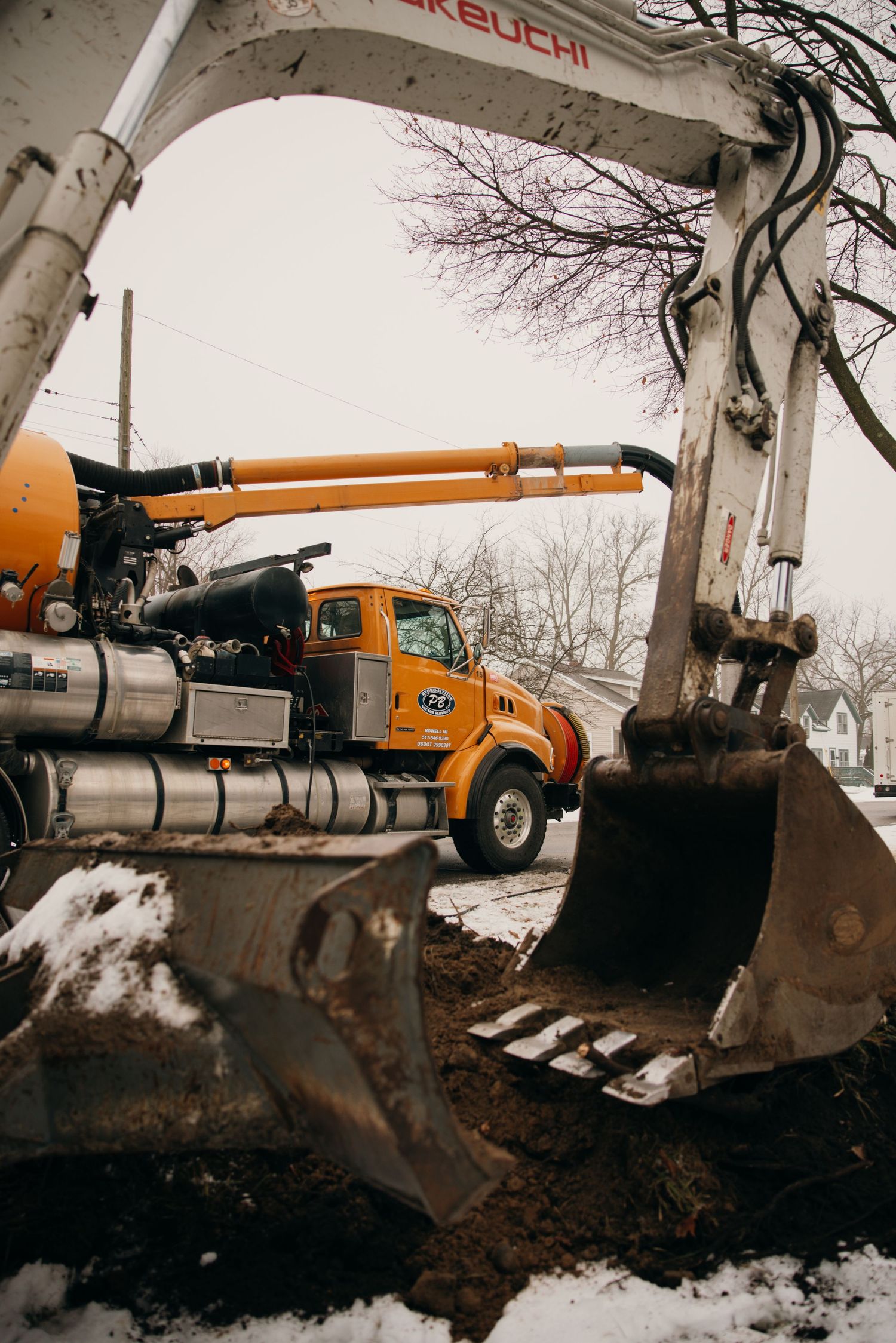 Heavy construction equipment including excavator and orange truck working in snowy conditions.