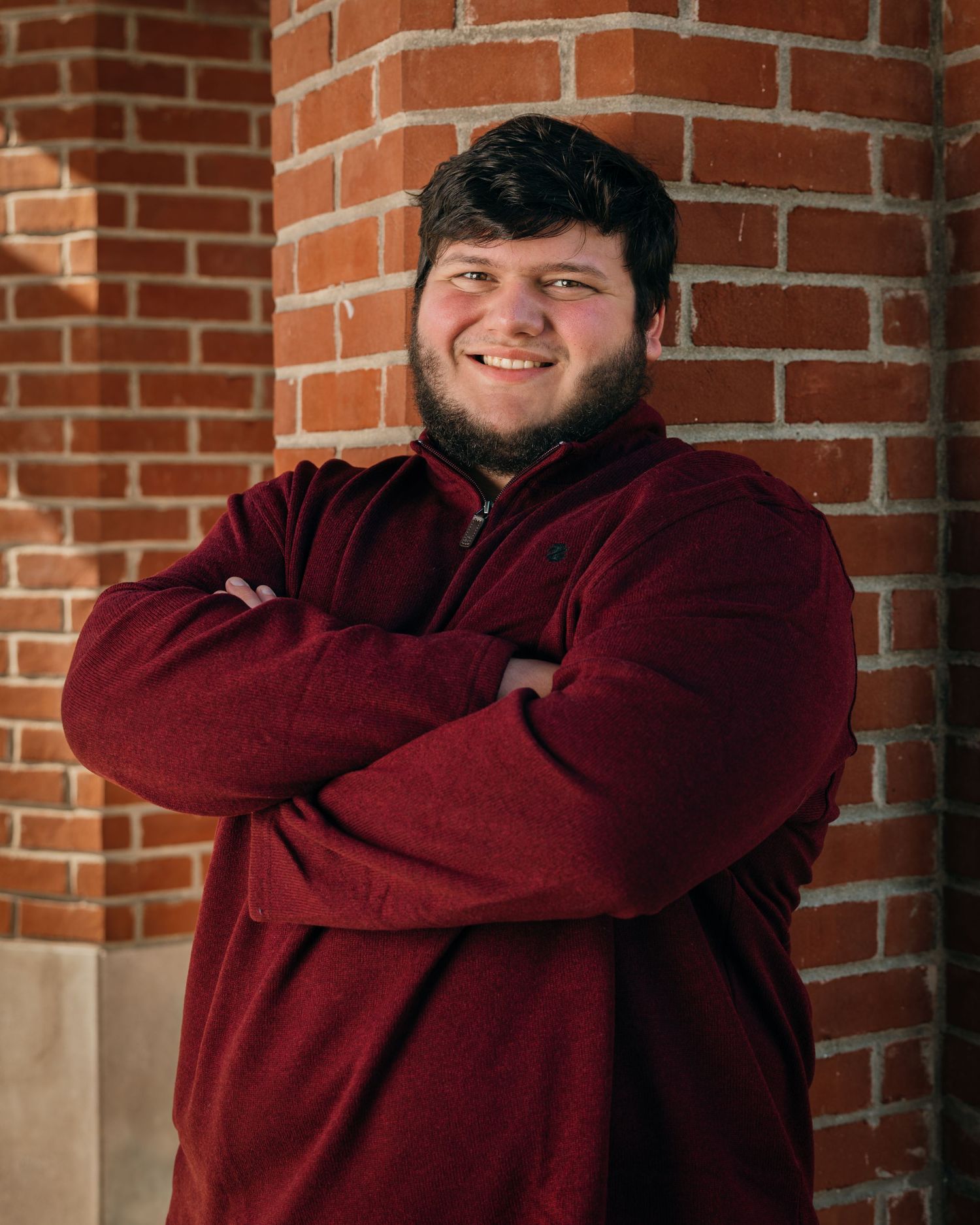 Professional portrait series against a brick wall wearing a burgundy hoodie.