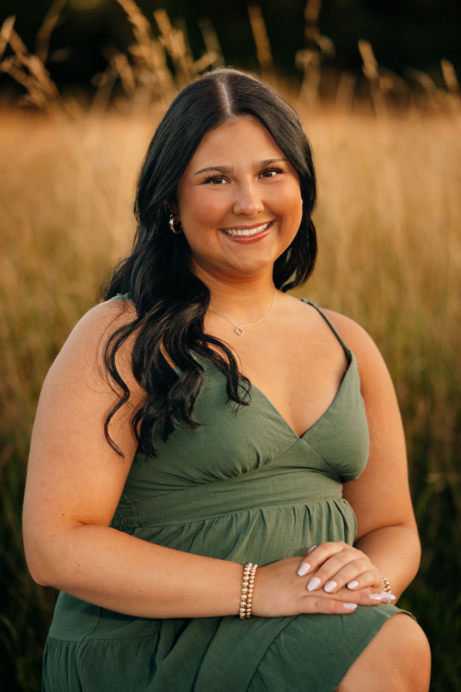 Person in green dress poses in golden field at sunset.