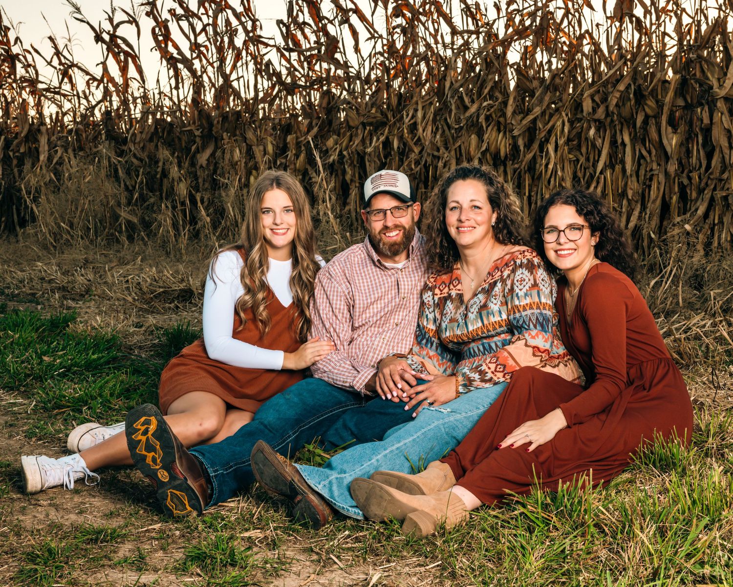 Family portrait with four people sitting together against a backdrop of dried corn stalks.