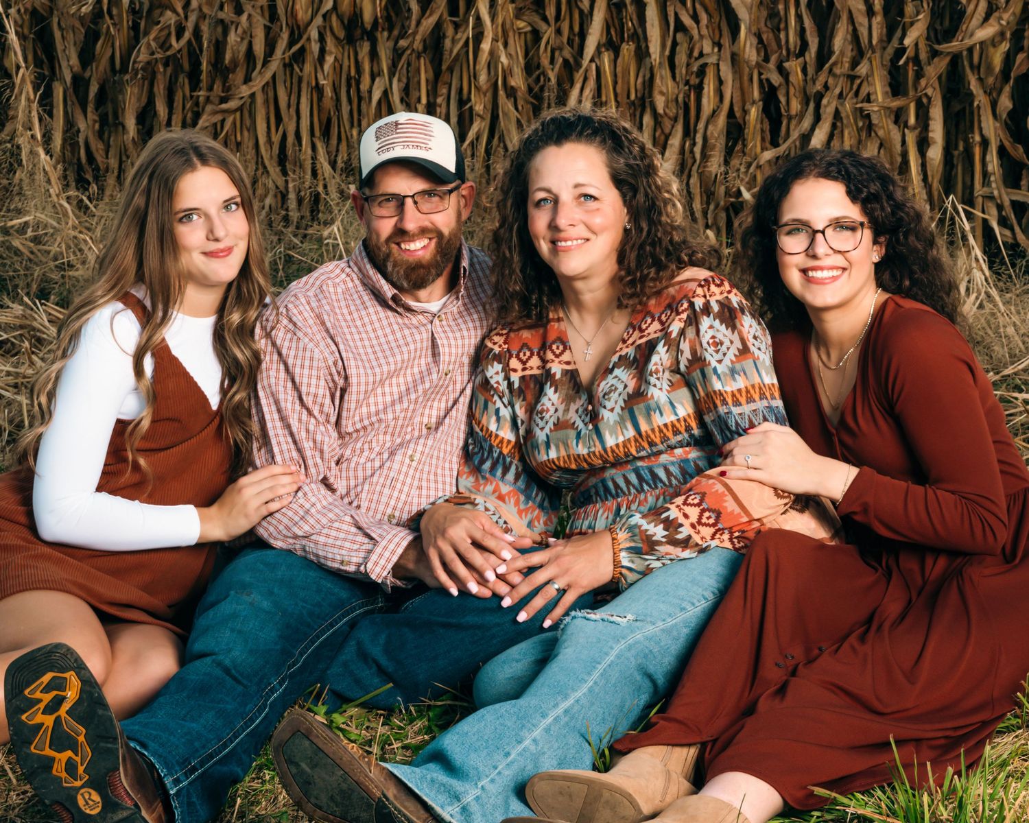 Family group photo taken in front of dried corn stalks during an autumn photoshoot.