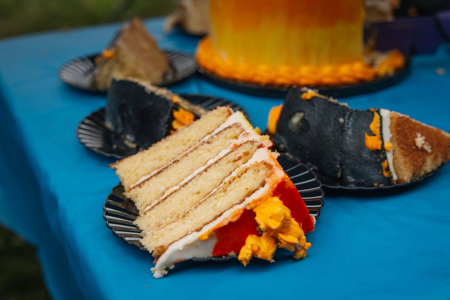 Layered vanilla cake slice with colorful garnish served on dark plates against blue tablecloth.