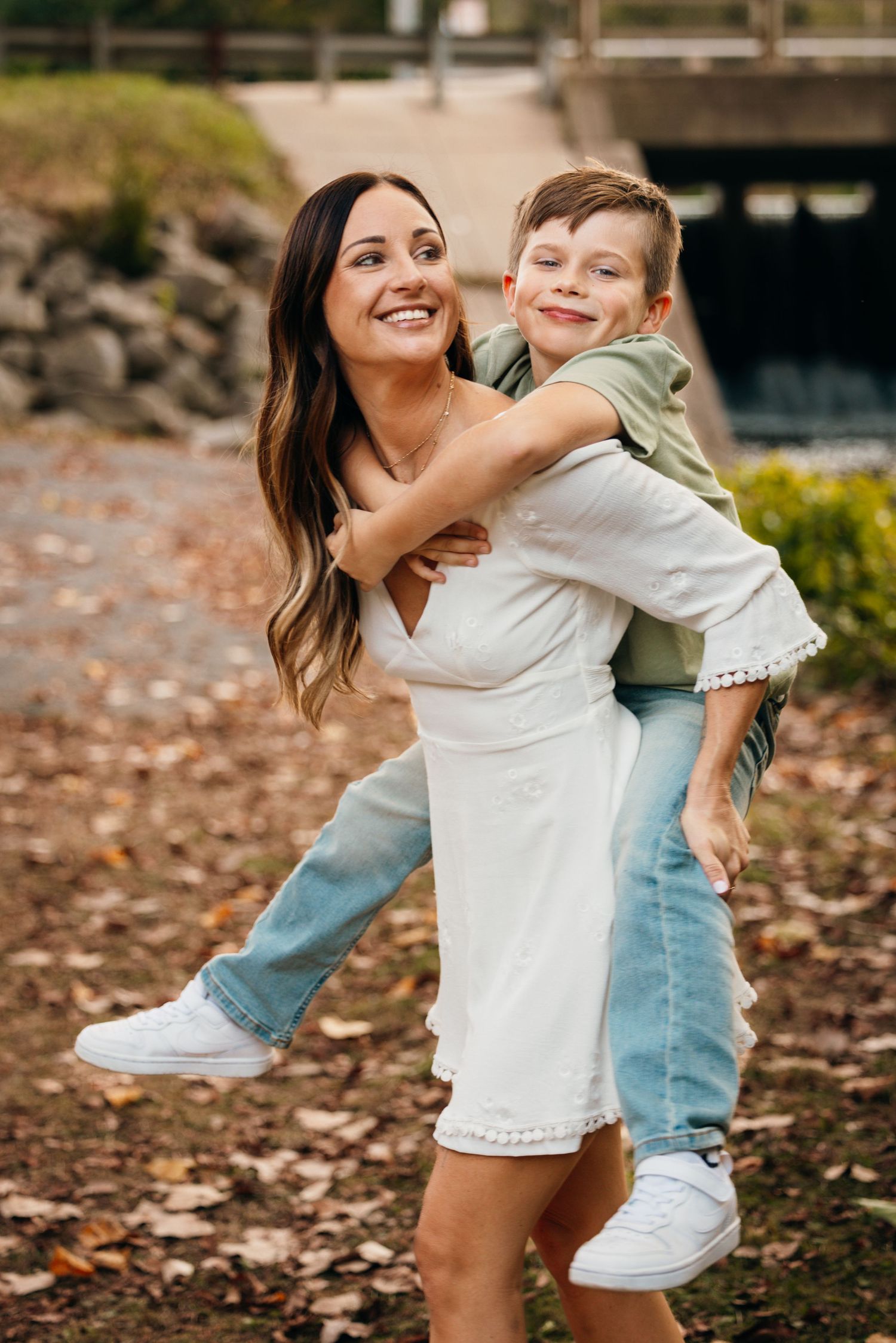 Playful moment captured outdoors with fall foliage and bridge in background.