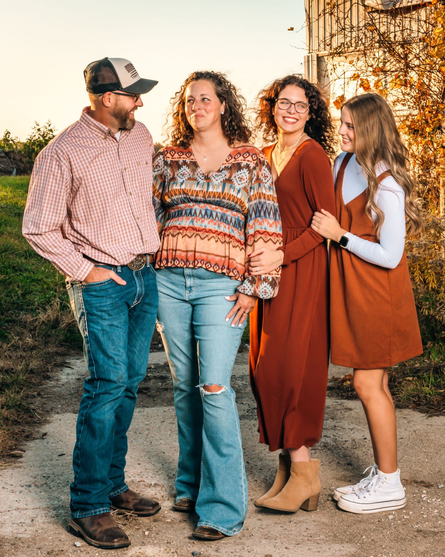 A casual family group poses together outdoors against a rustic metal wall at sunset.