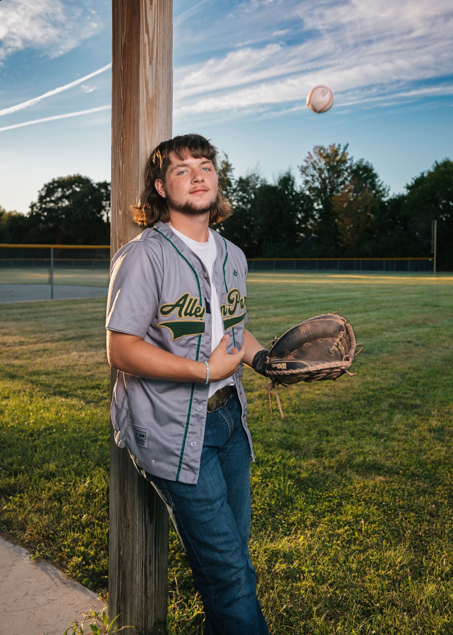 Baseball player practices catching drills on a field at sunset.