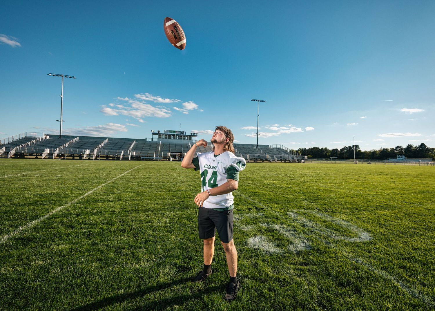 Football players practice on sunny field with blue sky overhead.