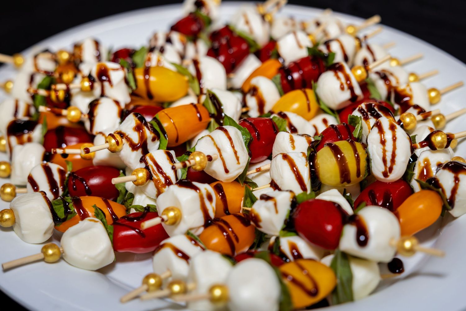 Colorful caprese skewers with mozzarella, tomatoes and balsamic drizzle arranged on a white plate.