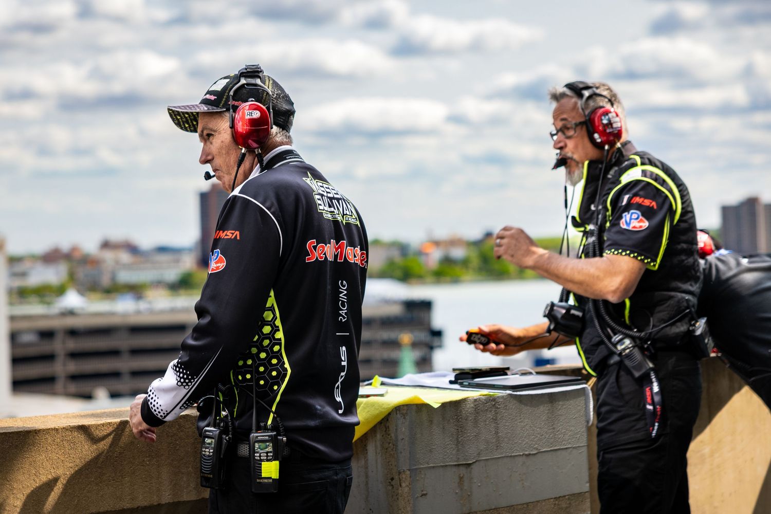 Racing team members in black uniforms discussing strategy on pit wall.