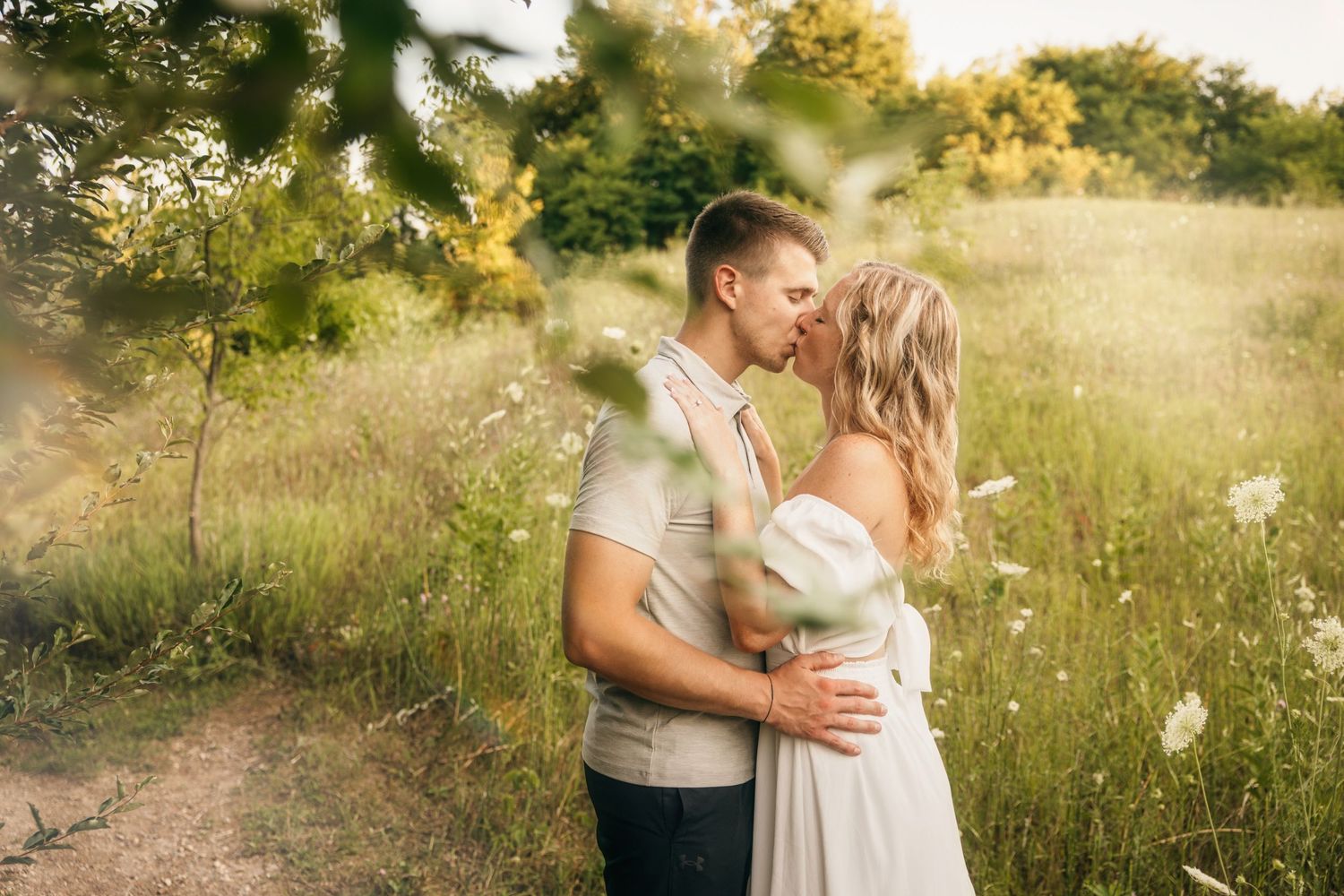 Romantic couple embraces in a sunlit meadow during golden hour with wildflowers in the background.