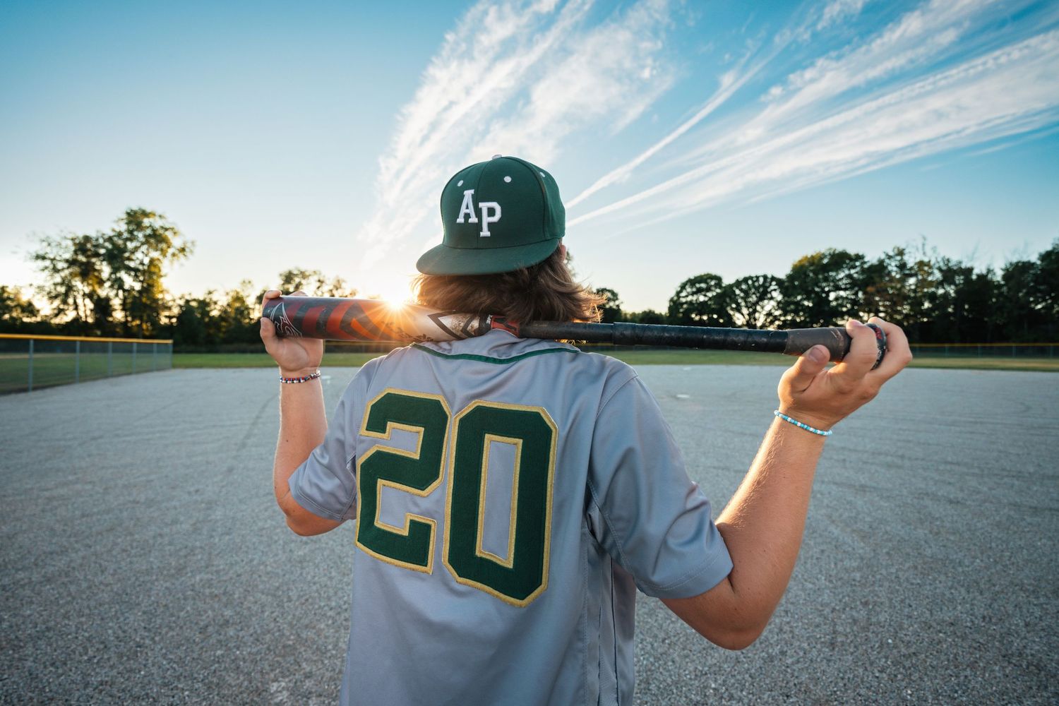 Baseball player in green uniform stands against blue sky backdrop.