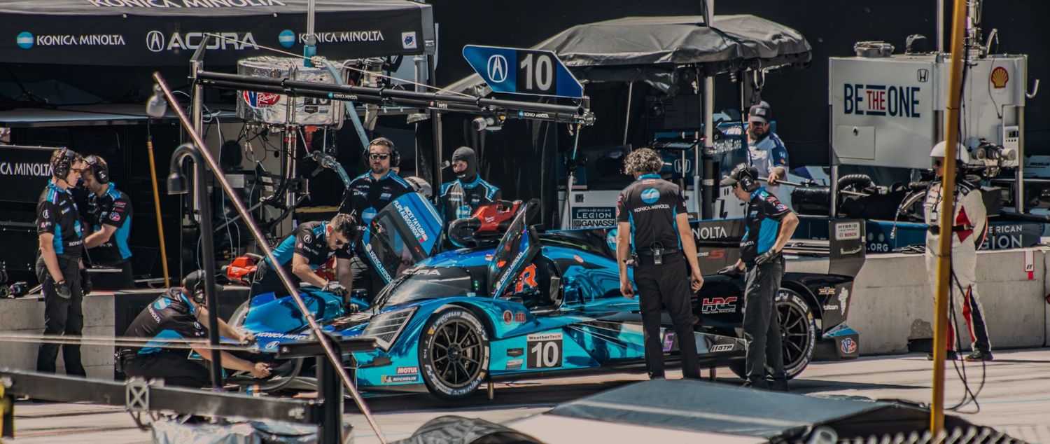 Racing pit crew working on blue race car during pit stop maintenance.