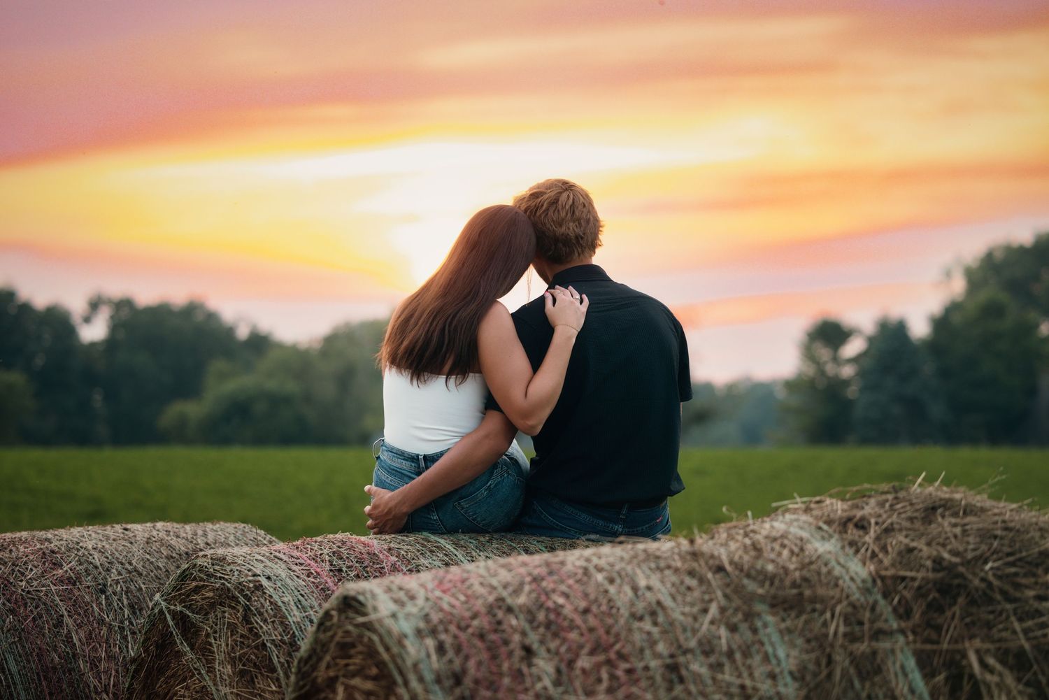 Silhouettes sitting on hay bales against a vibrant sunset sky.