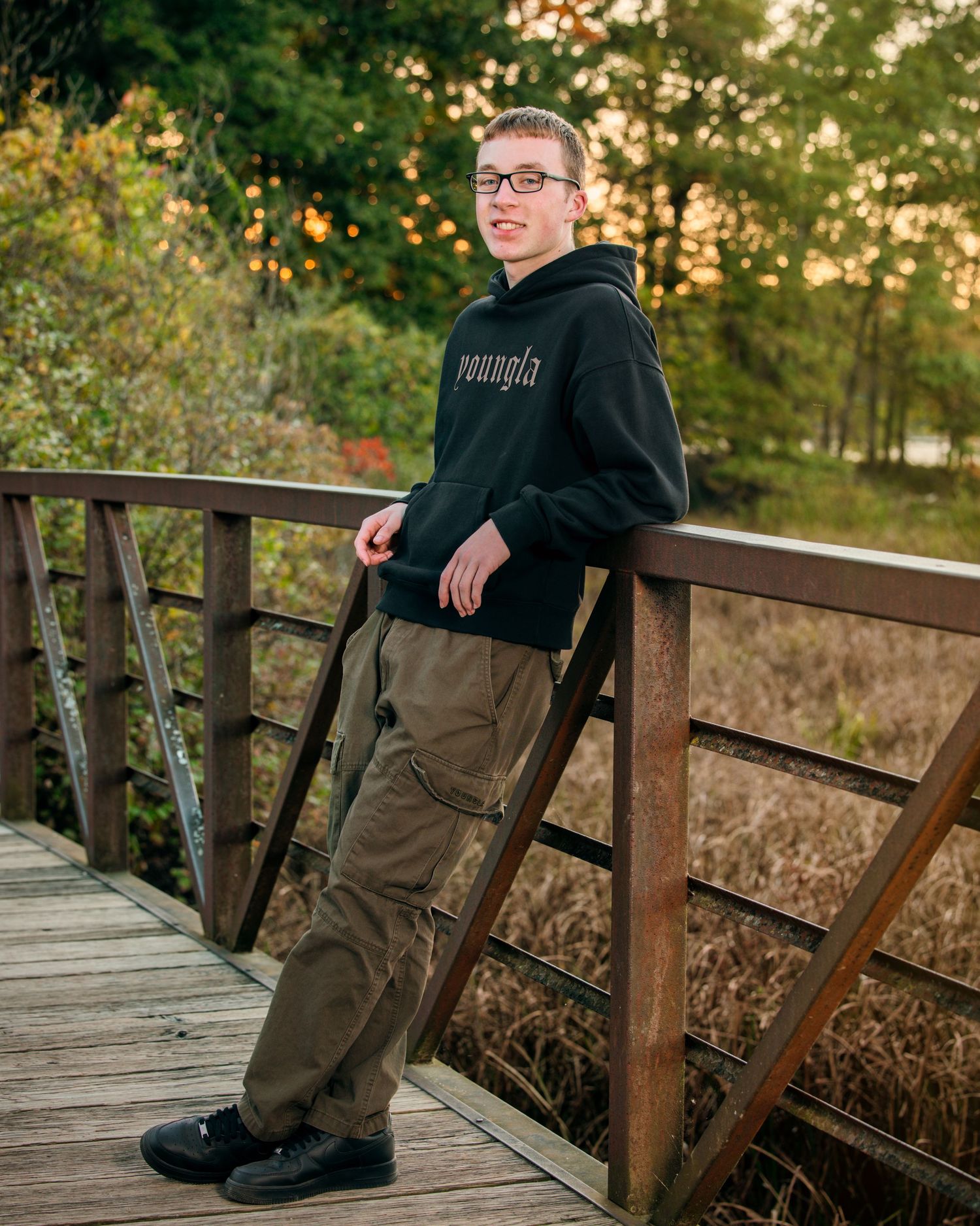 Person sitting on wooden boardwalk wearing dark sweatshirt and cargo pants during sunset.