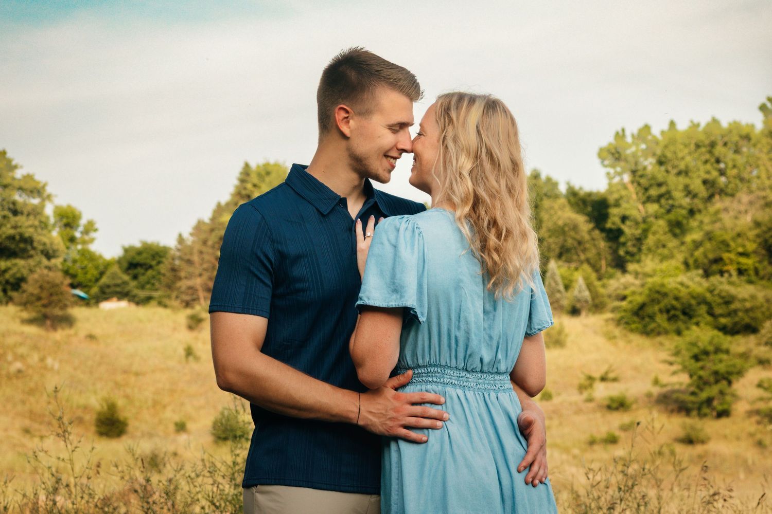 Couple in casual attire sharing tender moment in sunlit meadow.