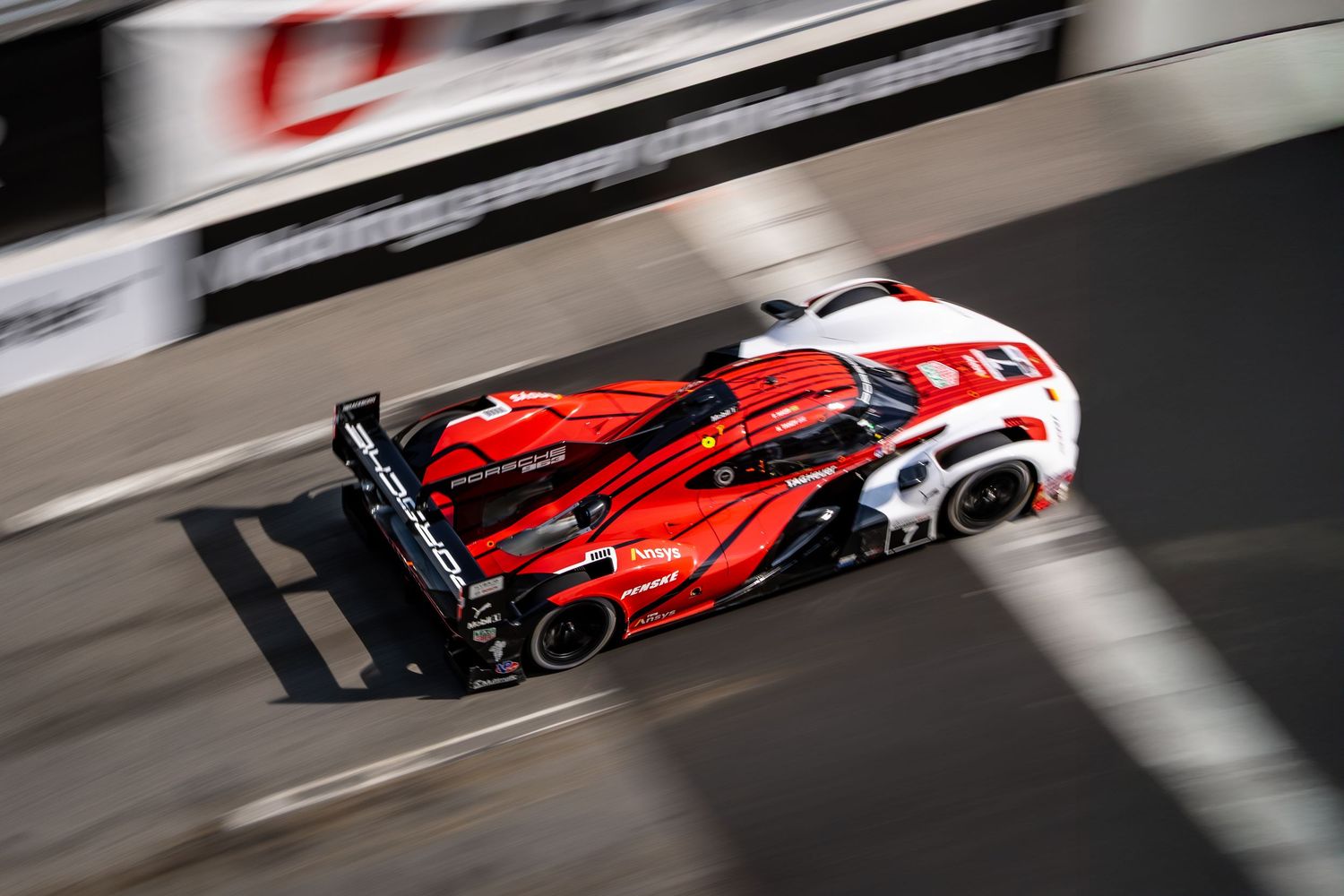Red and white Formula 1 race car speeding past on track with motion blur effect.