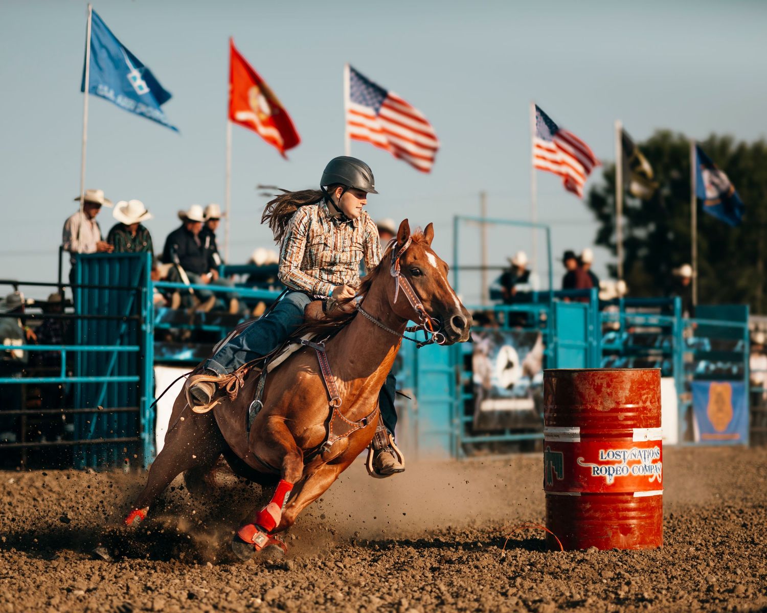 Horse and rider race past orange barrels during rodeo barrel racing competition.
