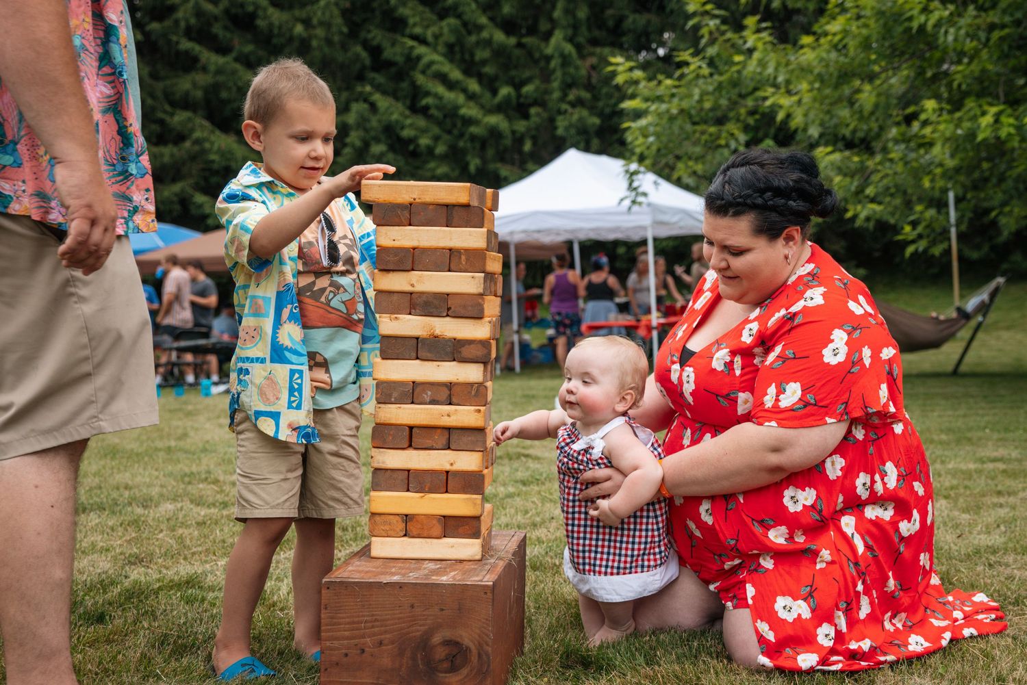 People playing giant Jenga game outdoors at summer gathering.