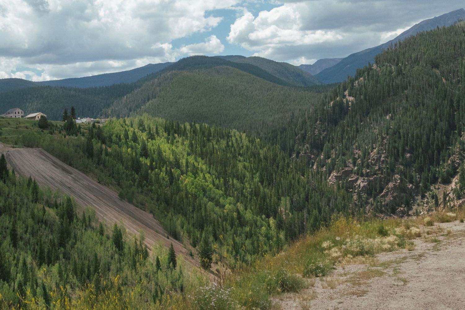 Panoramic mountain view with dense forest and winding road through valley.