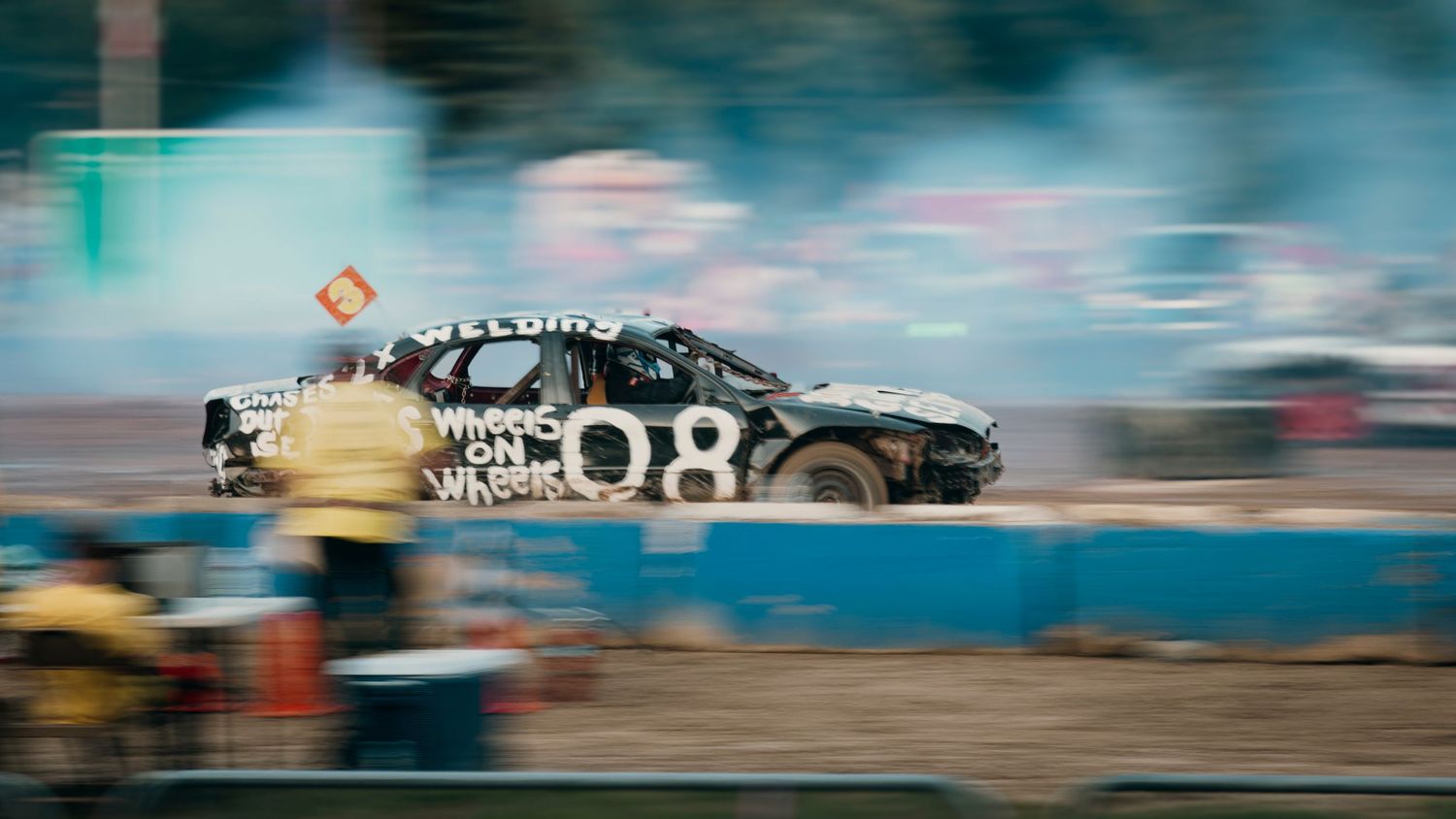 Motion-blurred racing cars speeding past on a racetrack with dramatic lighting.
