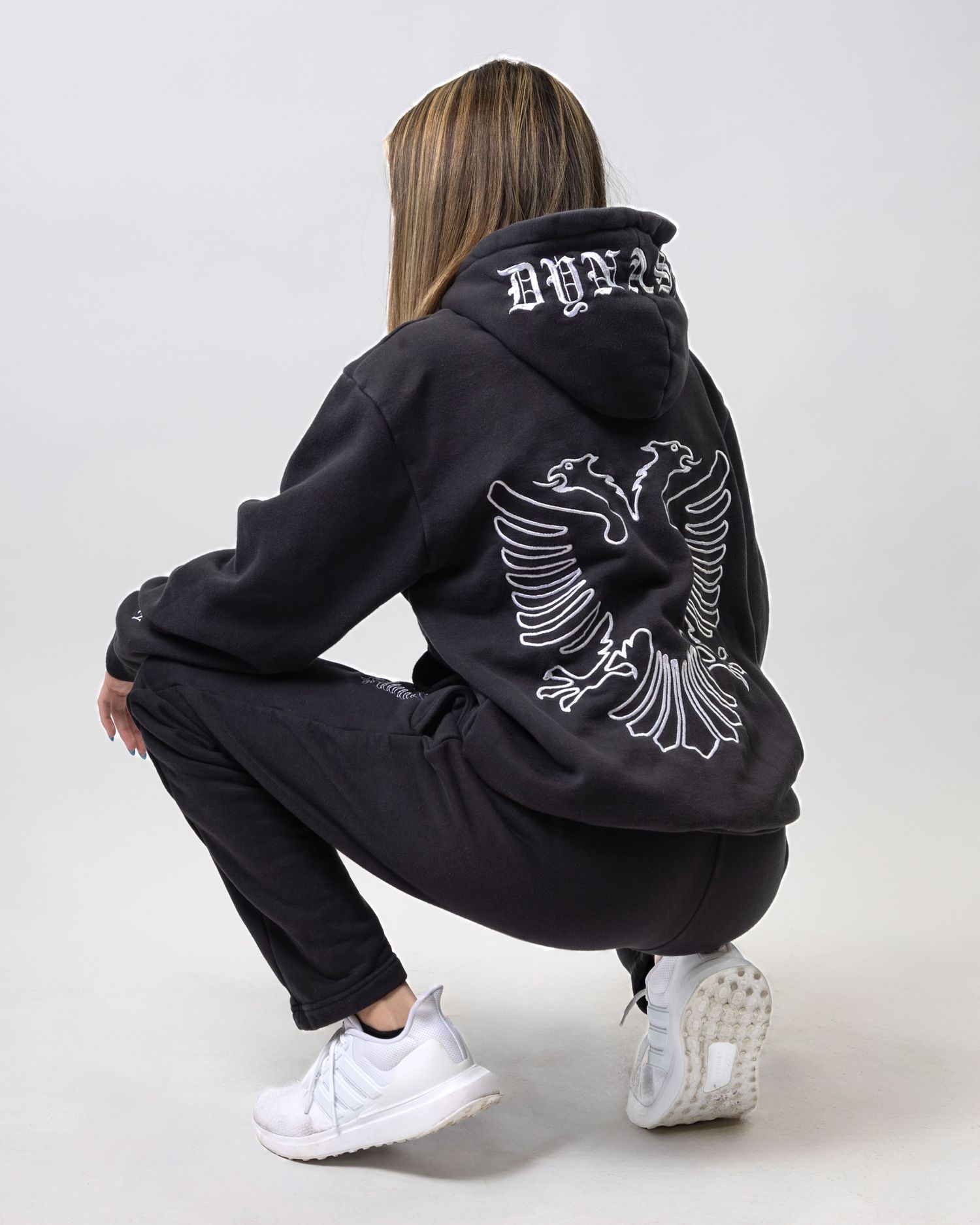 Black hoodie with eagle design shown from back view on model in squatting position.