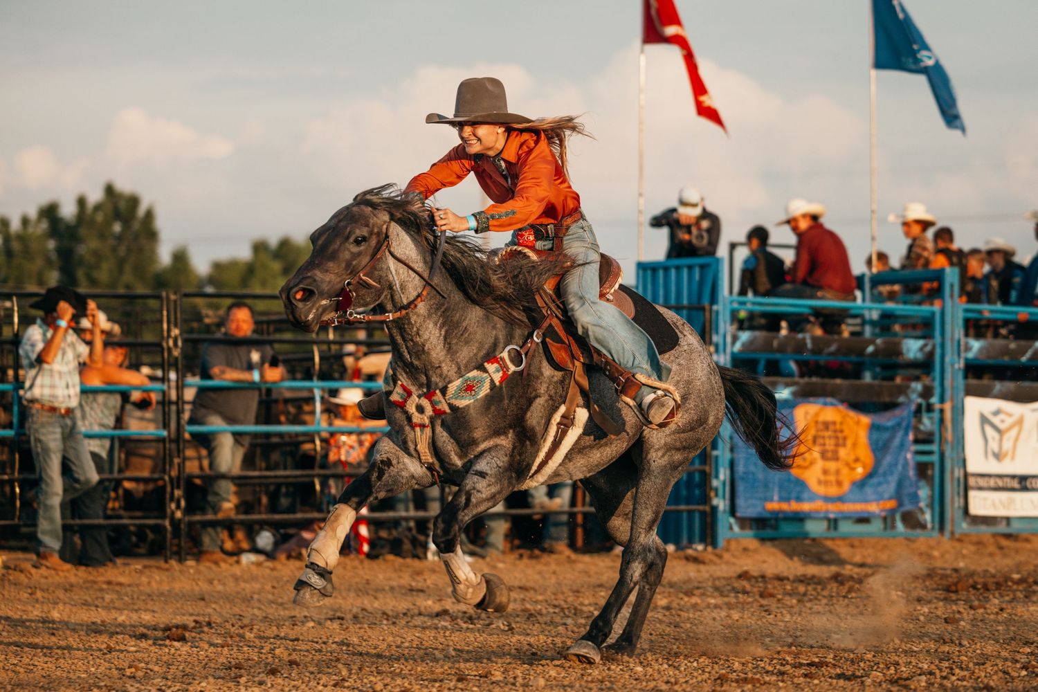 Rodeo competitors race through the arena with flags flying in the background.