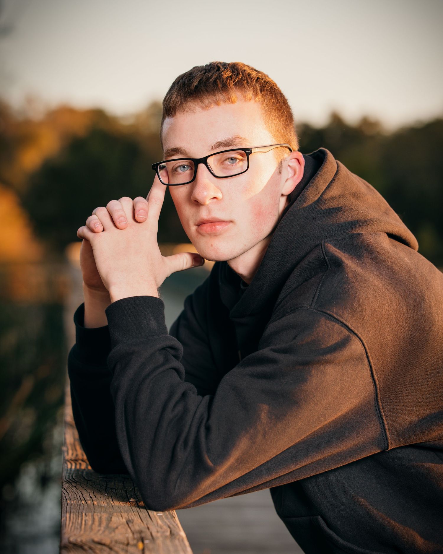 Close-up portrait with warm sunset lighting and dark hoodie against blurred background.