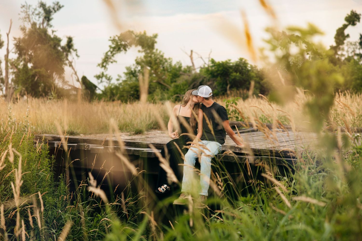 Couple sitting on vintage truck in tall grass during golden hour.