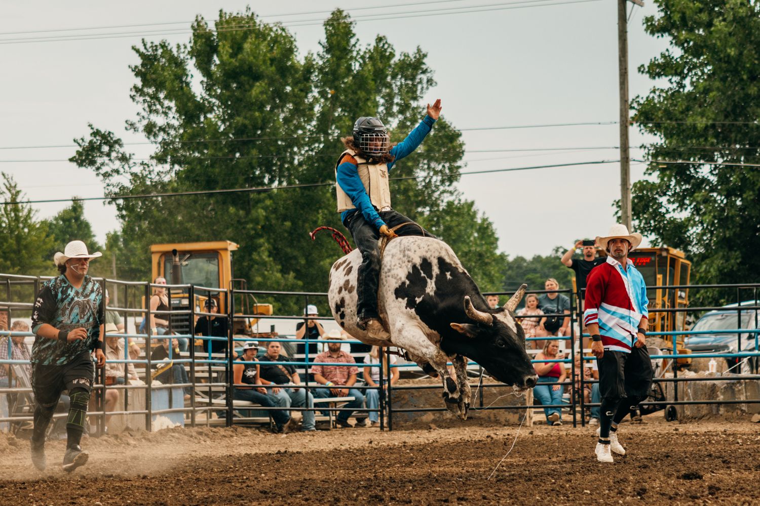 Action shot of rodeo bronc riding with spectators watching from the fence.