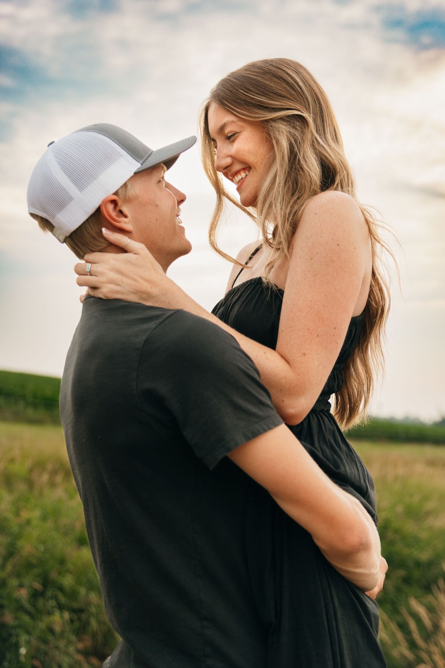 Couple sharing tender moment in field against cloudy sky.