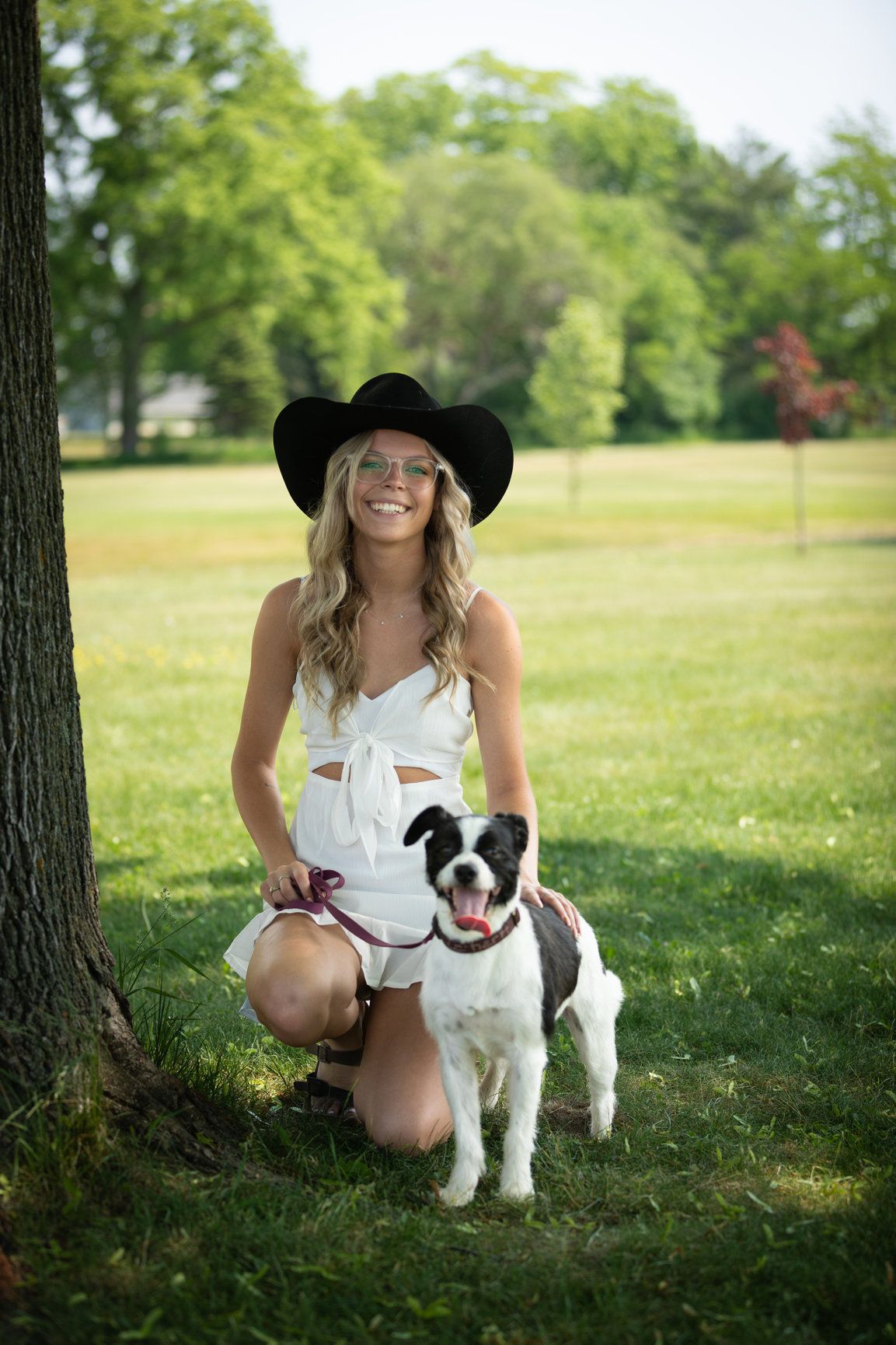 Black and white dog posing with owner under shaded trees in a grassy park.