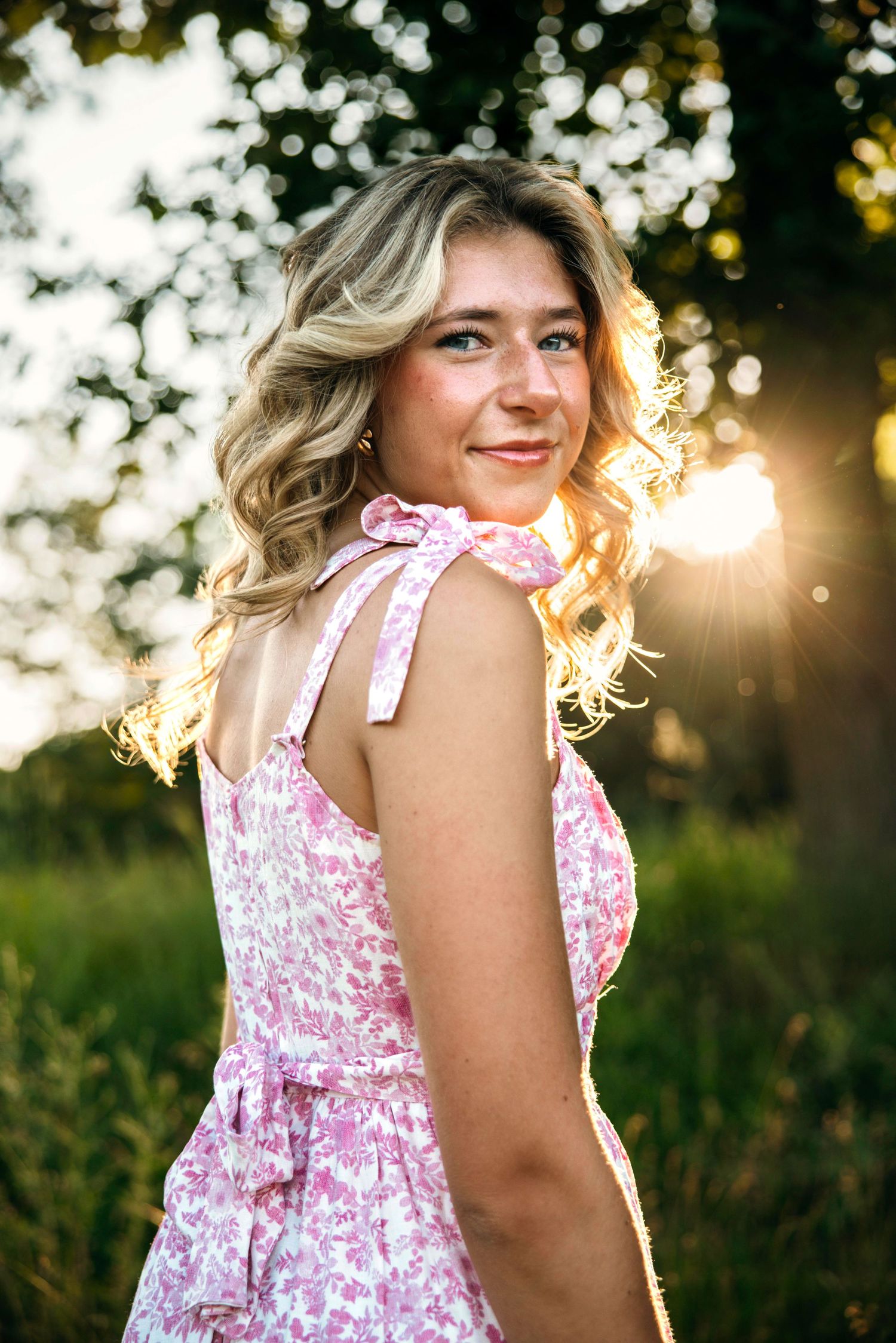 Portrait of a person in a pink floral dress with shoulder ties backlit by golden sunlight.
