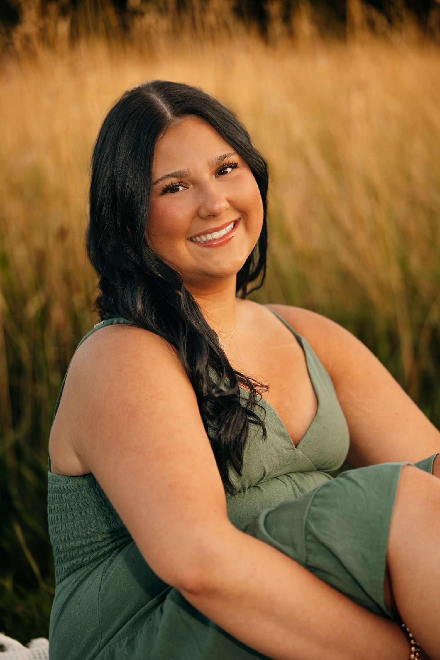 Person in olive green dress poses in tall grass during golden hour.