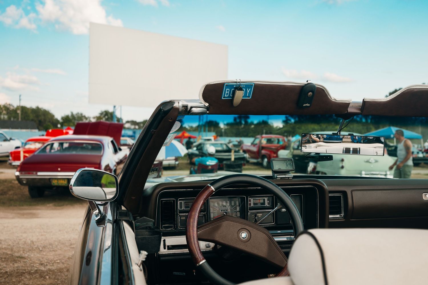 Panoramic view of cars parked at an outdoor event under bright blue sky.