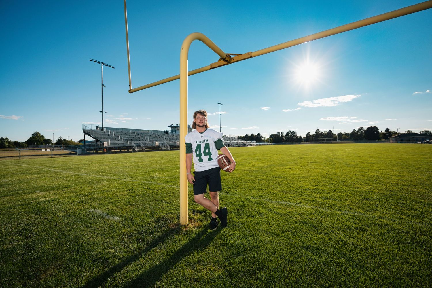 A football field with goal posts and green grass stretches out under a bright blue sky.