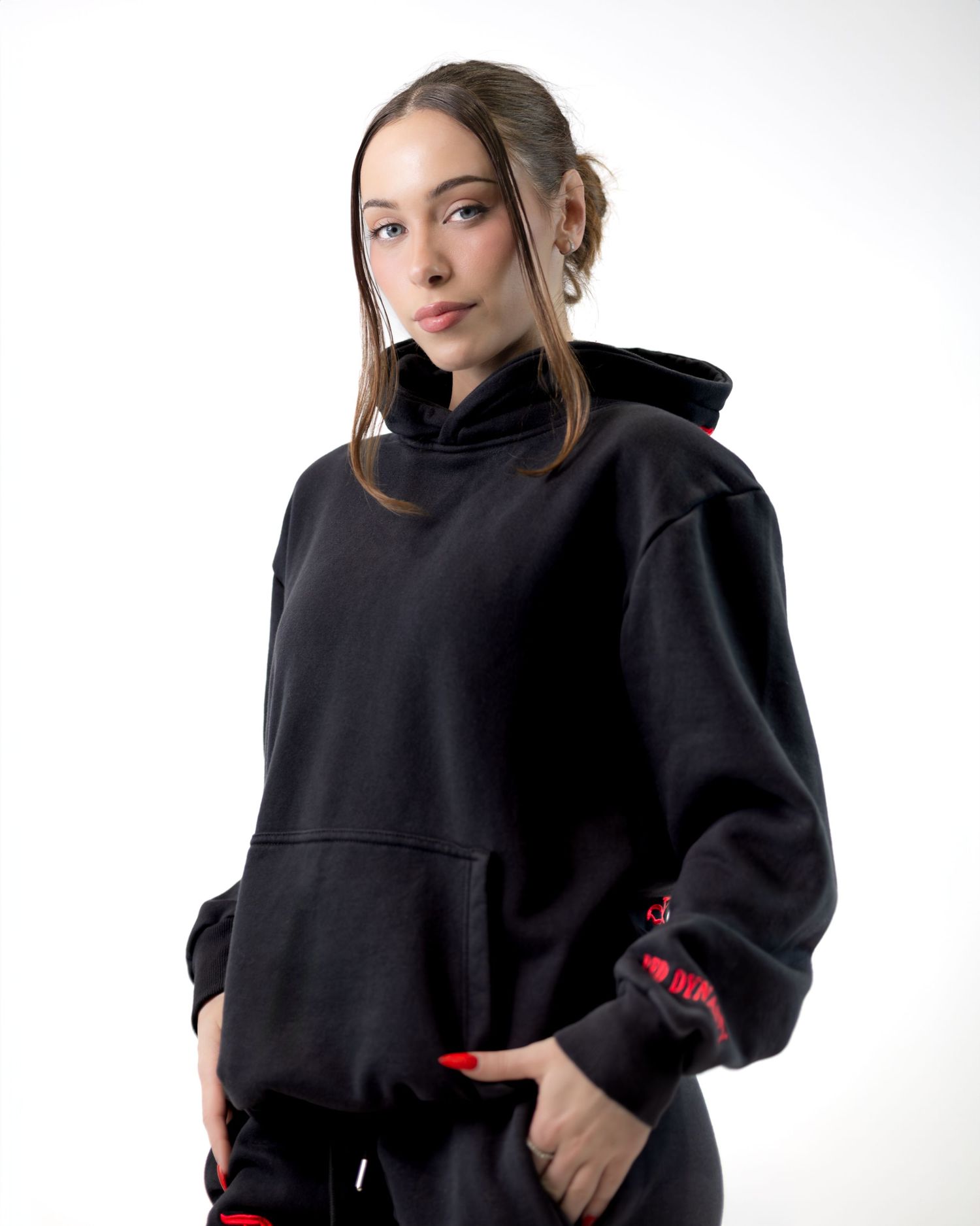 Fashion model posing in black sweatshirt with red accents against white backdrop.