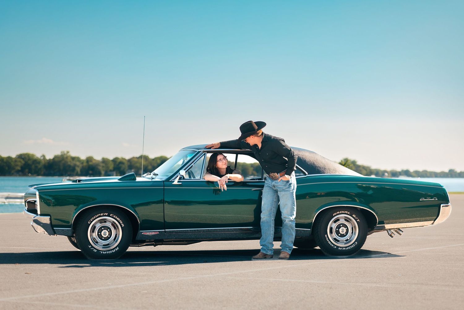 Classic green muscle car photoshoot on empty parking lot near water.