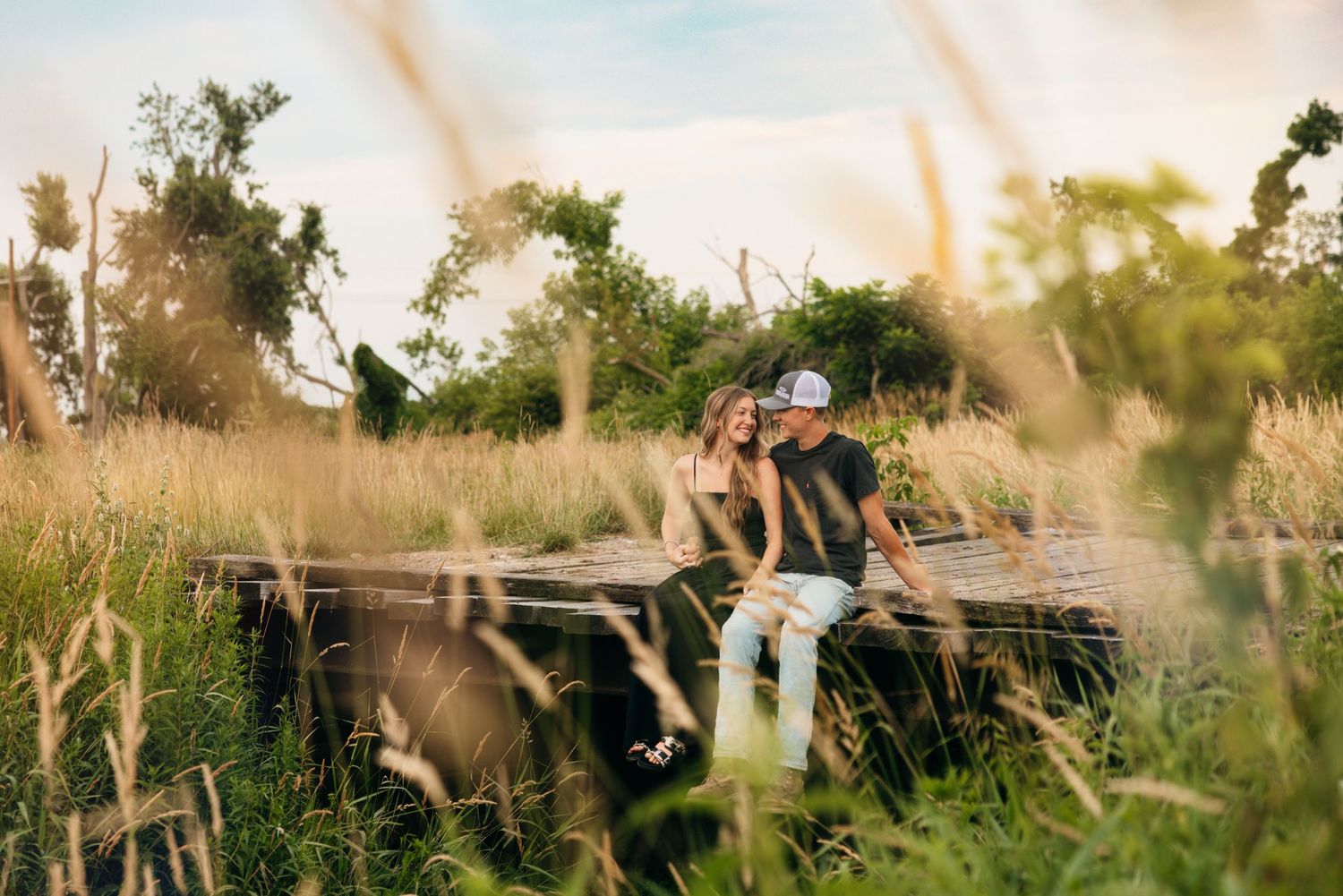 Silhouetted couple embraces in a golden sunset field with tall grass and trees in the background.