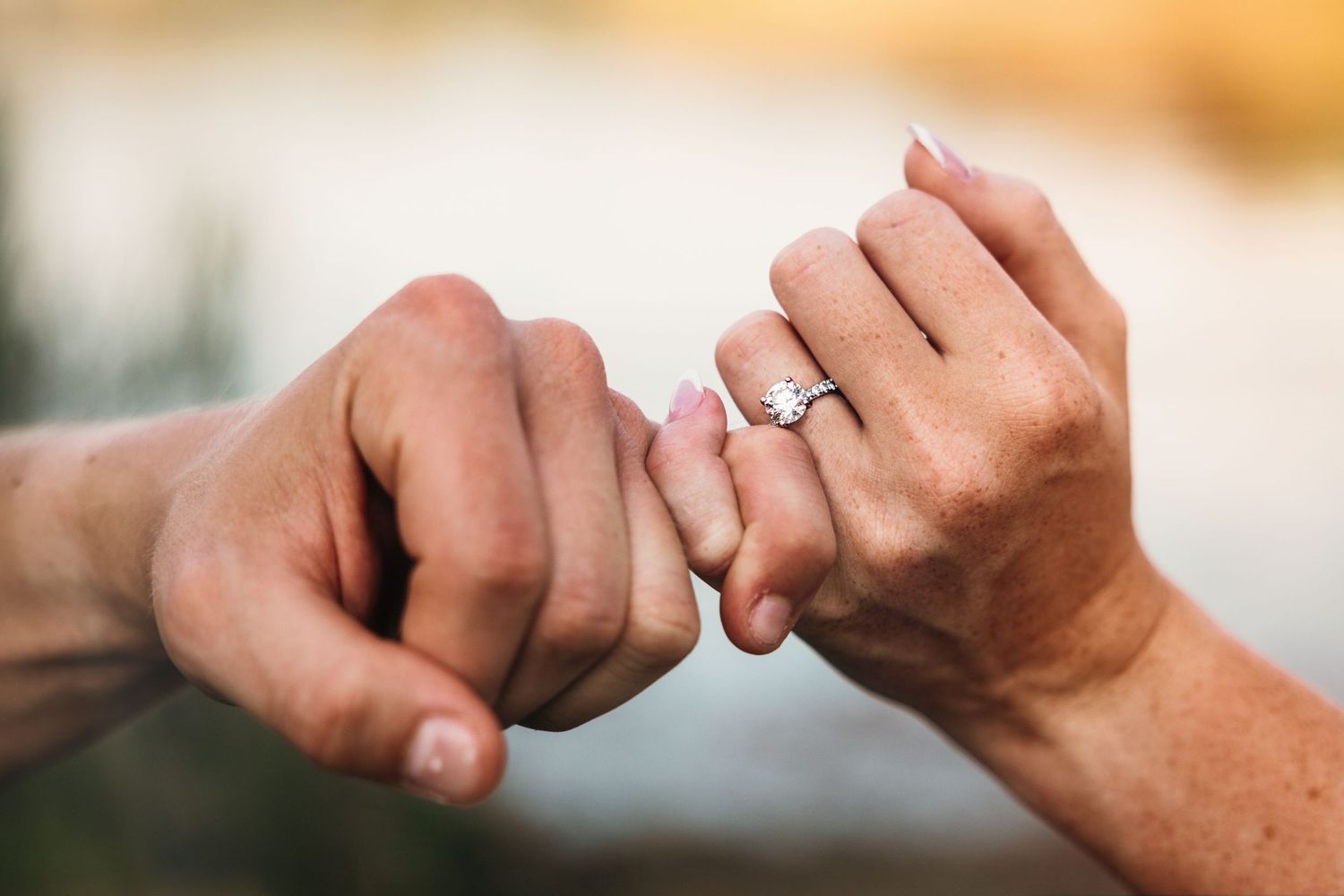 Close-up of two hands with fingers intertwined showing off an engagement ring.